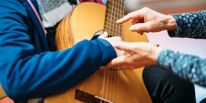 Kind mit Gitarre, Lehrerin korrigiert die Handstellung