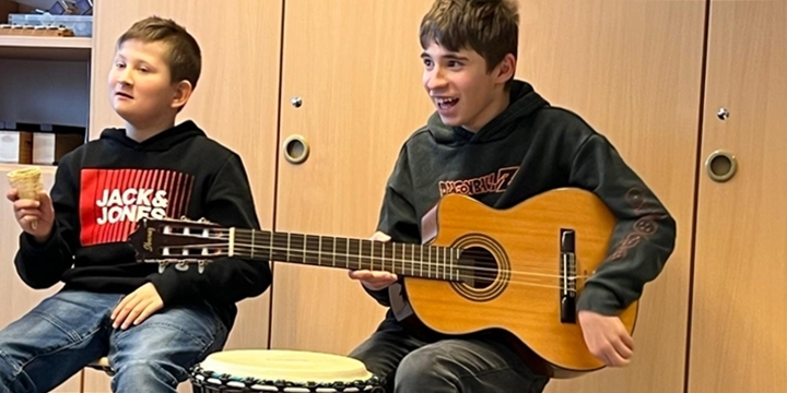 Zu sehen sind 2 Jungen, der eine spielt Gitarre und lacht, der andere hat in der Hand einen kleinen Shaker zum Musik machen  ©MKS